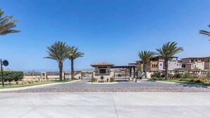 Una entrada amurallada con un monumento central, palmeras y edificios de arquitectura mediterránea.