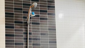 Una ducha con un rociador de manguera y un cabezal de ducha manual en una pared de azulejos.