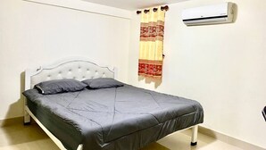 Un dormitorio con cama, cabecera blanca, aire acondicionado de pared y cortina.