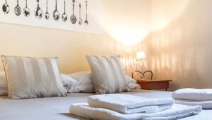 A neatly made bed with white pillows and folded towels, a bedside table with a lamp, and a wall with spoon illustrations. - Reinassance Beauty - elegant apartment in the heart of Florence (Firenze)