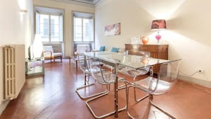 A spacious room with a glass-top dining table surrounded by clear chairs, a wooden cabinet, and a radiator. - Reinassance Beauty - elegant apartment in the heart of Florence (Firenze)