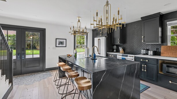 A modern kitchen with a large island, bar stools, a chandelier, and a view of the outdoors. - Unwind in Style | The Longboard (Mount Pleasant)