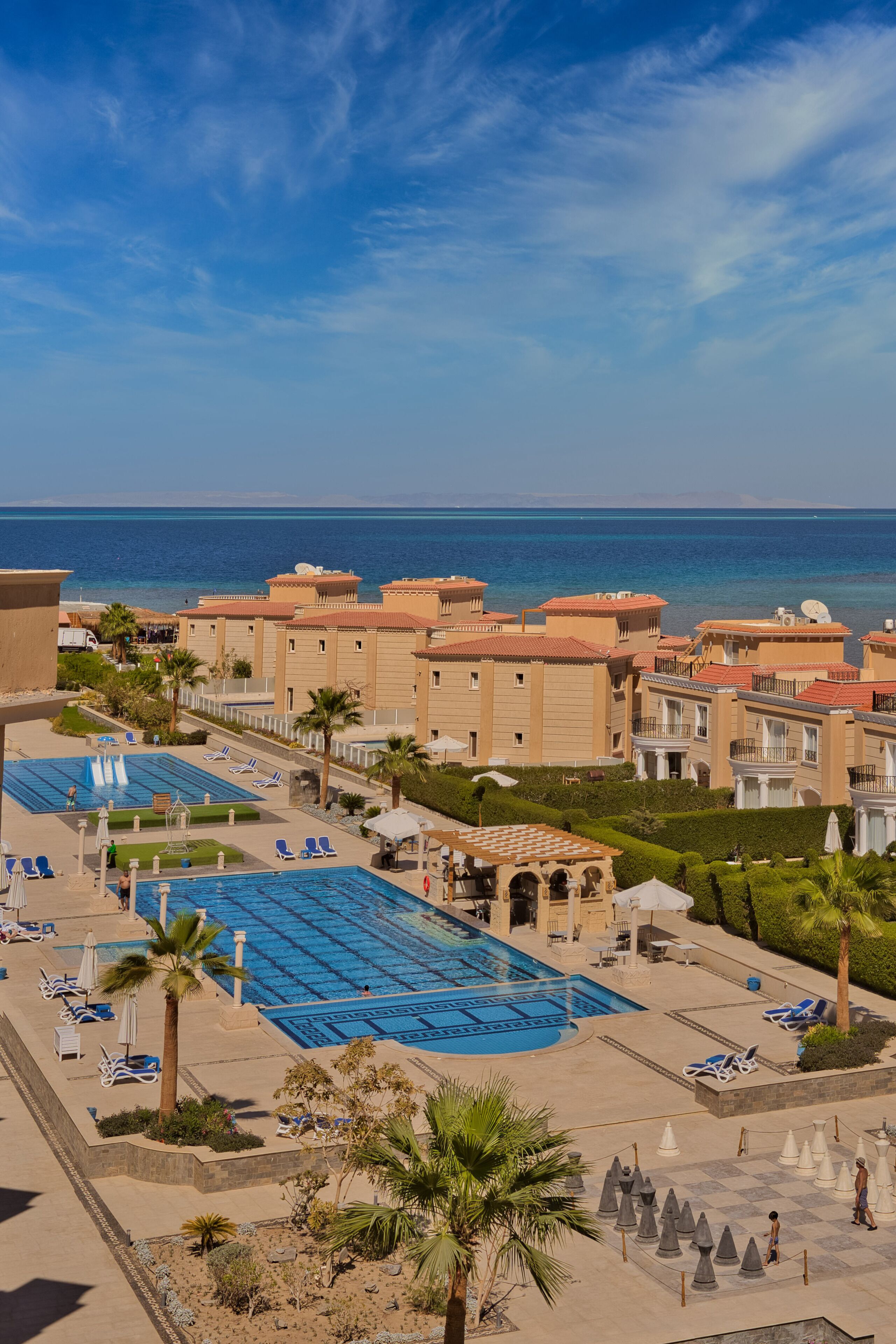 Un resort con varias piscinas, palmeras y vista al mar.