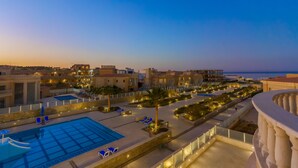 A rooftop pool area with multiple pools, lounge chairs, and a view of the cityscape at dusk. - Selena Bay Resort (Hurghada)