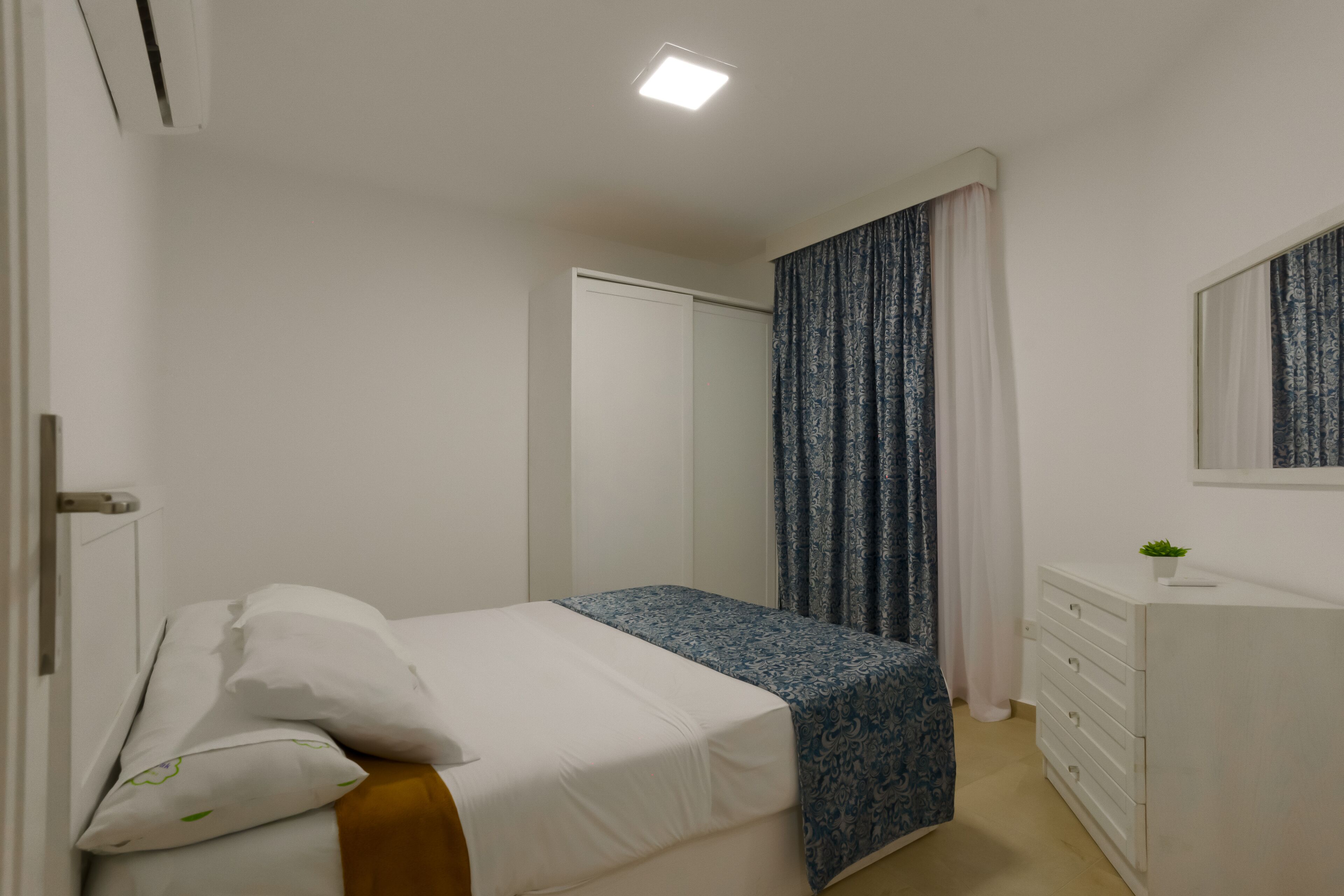 A bedroom with a bed, a dresser, a mirror, and a door.