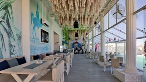 A restaurant with long communal tables and chairs, large windows, and hanging plants. - Selena Bay Resort (Hurghada)