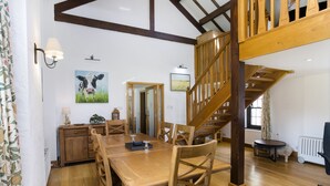 A spacious dining area with a wooden table and chairs, a staircase with wooden railings, and a view of the kitchen in the background. - Keiras Cottage - Three Bedroom House, Sleeps 6 (Ambleside)