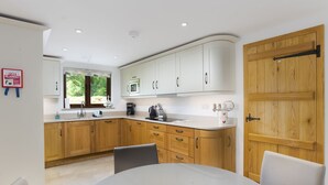 A modern kitchen with white cabinets, a wooden door, and a dining area with a white table and chairs. - Keiras Cottage - Three Bedroom House, Sleeps 6 (Ambleside)