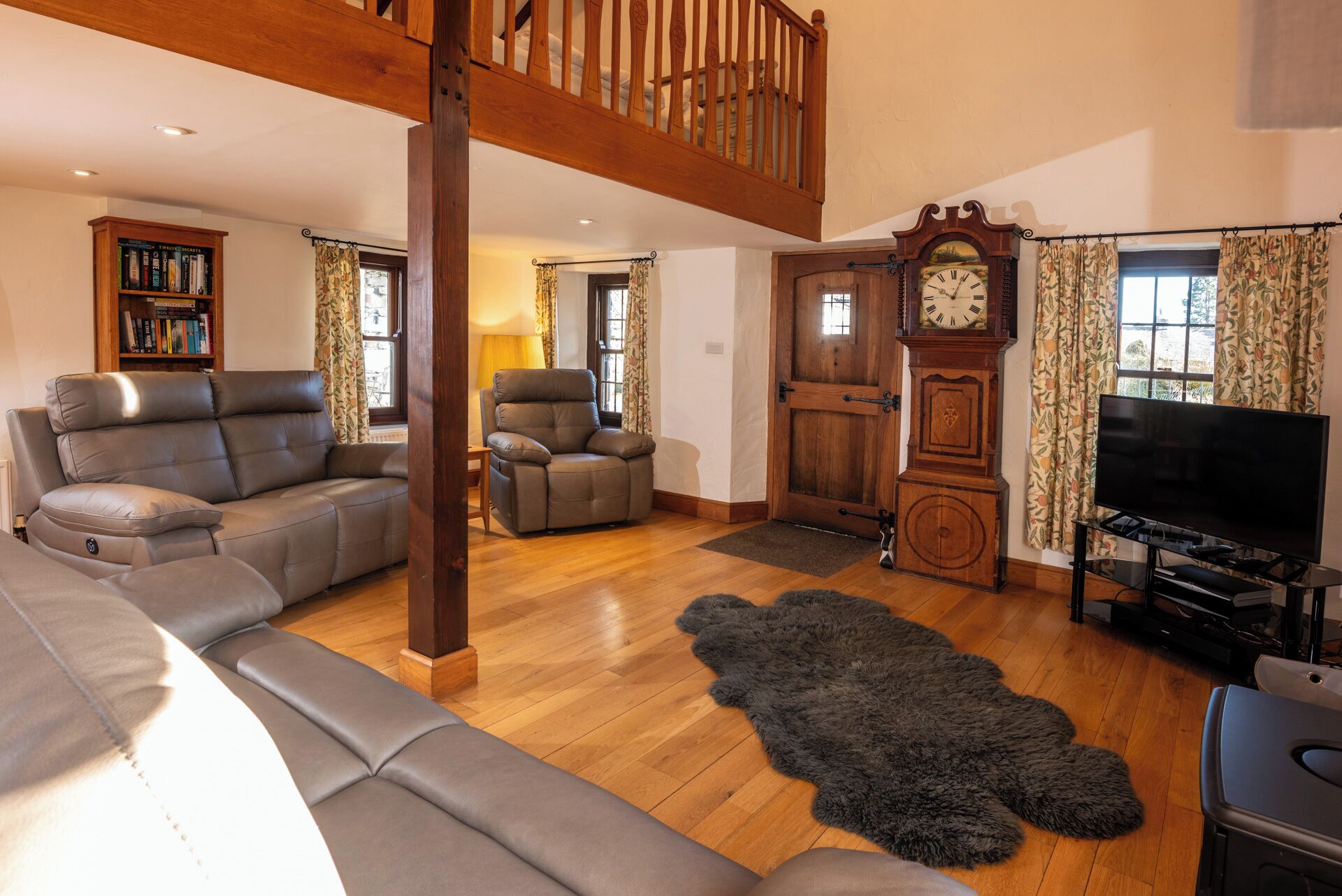 Un salón espacioso con un alto techo de madera, un amplio sofá de cuero, un sillón reclinable, un reloj de madera y un televisor.