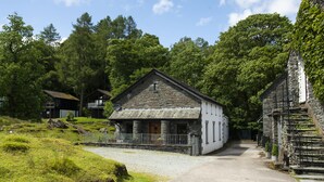 A stone building with a white facade, a gravel driveway, and surrounding greenery. - Keiras Cottage - Three Bedroom House, Sleeps 6 (Ambleside)