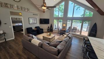 Un vaste espace de vie comprenant un grand canapé, une table basse et une table à manger avec des chaises. Un téléviseur est fixé au mur et un ventilateur de plafond est installé.