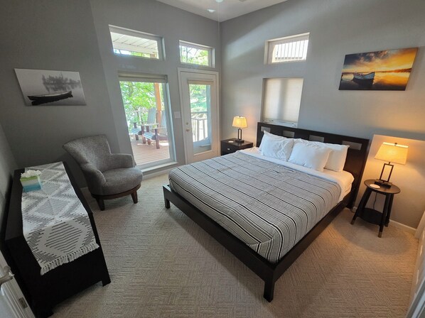 A bedroom with a bed, a chair, a nightstand, a lamp, and a view of the outdoors through a glass door.