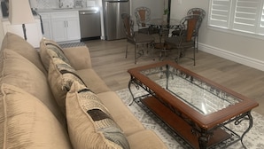Un salon comprenant un canapé, une table basse avec un plateau en verre et un coin repas avec des chaises et une table.