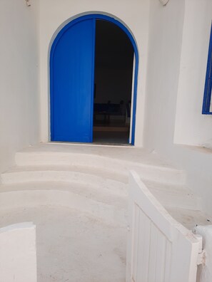 A white building with a blue door and white steps leading to a dark interior.