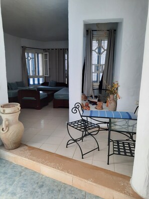 A room with a bed, a table with chairs, a vase with flowers, and a large pot.