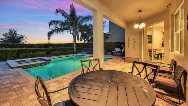 Zona junto a la piscina con una mesa y sillas, vista a la piscina y un atardecer al fondo.