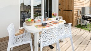 An outdoor patio with a white table and chairs, a basket of fruit, and a grill. - Soleil Couchant B03 by Interhome (Mimizan)