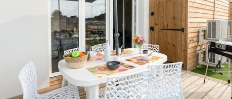 Eine Terrasse im Freien mit einem weißen Tisch und Stühlen, einem Obstkorb und einem Grill.