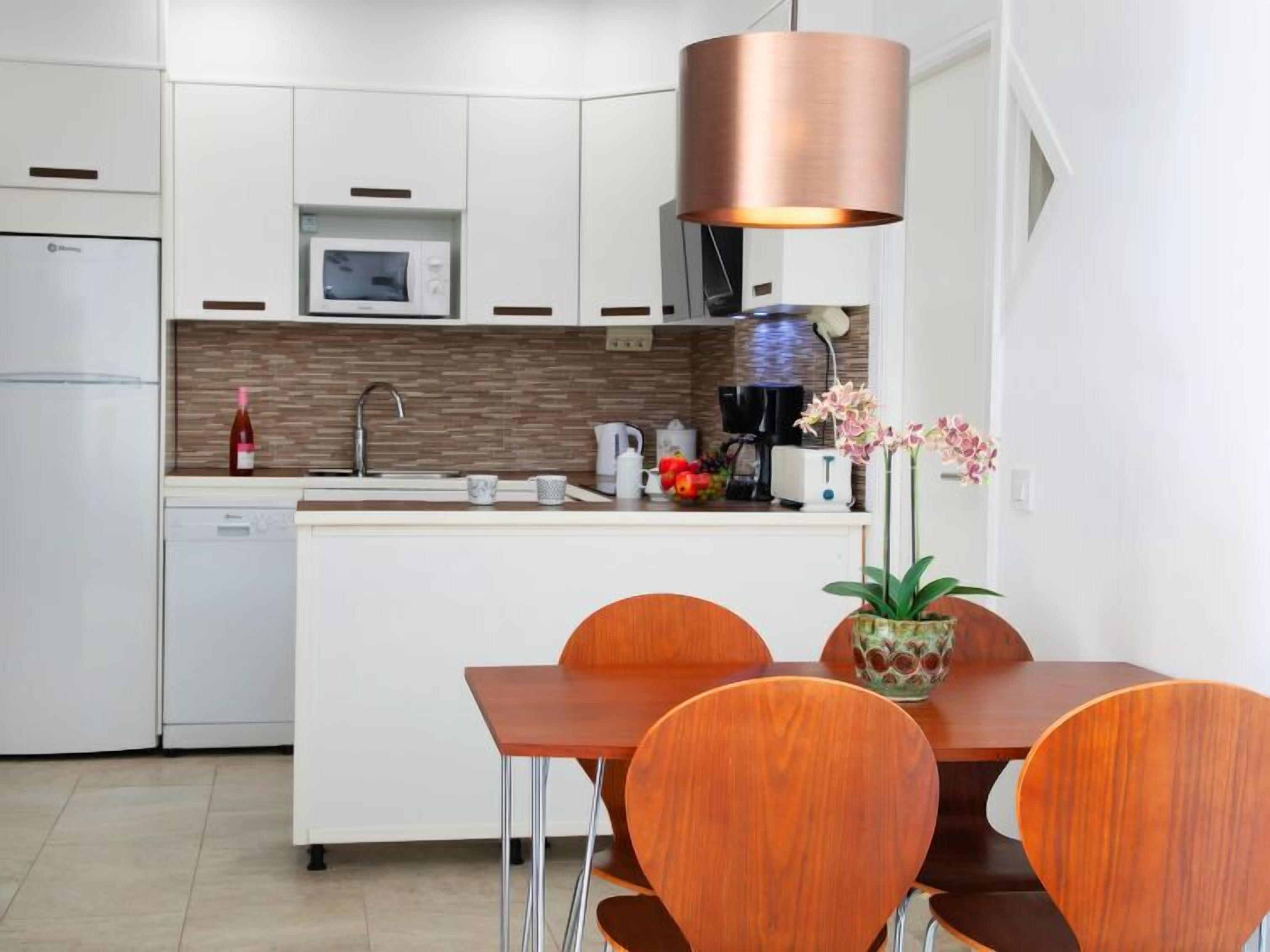 A modern kitchen with white cabinets, a built-in microwave, a coffee machine, and a dining area with a wooden table and chairs.