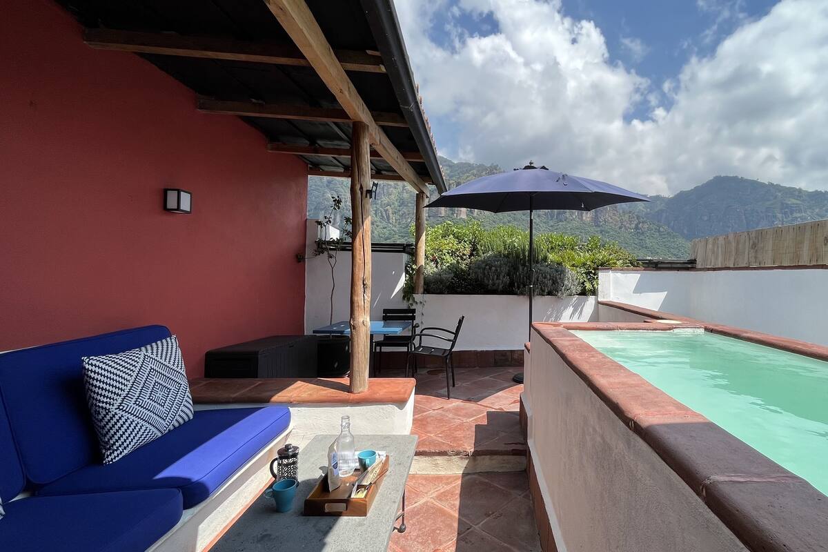 A patio with a pool, a blue sofa, and a table with a bottle and cups.