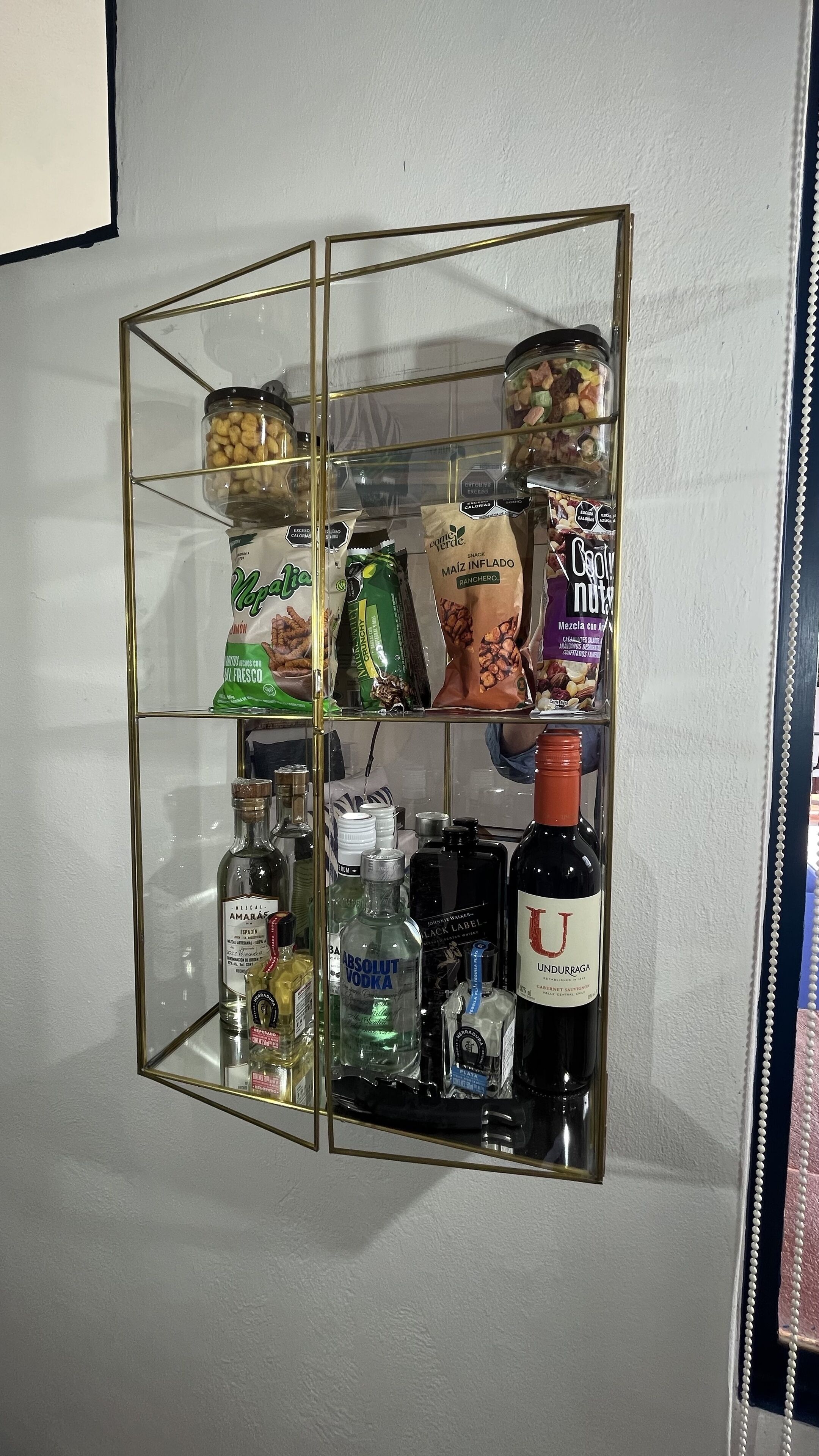 A glass-fronted, gold-framed shelf with various food items and bottles.