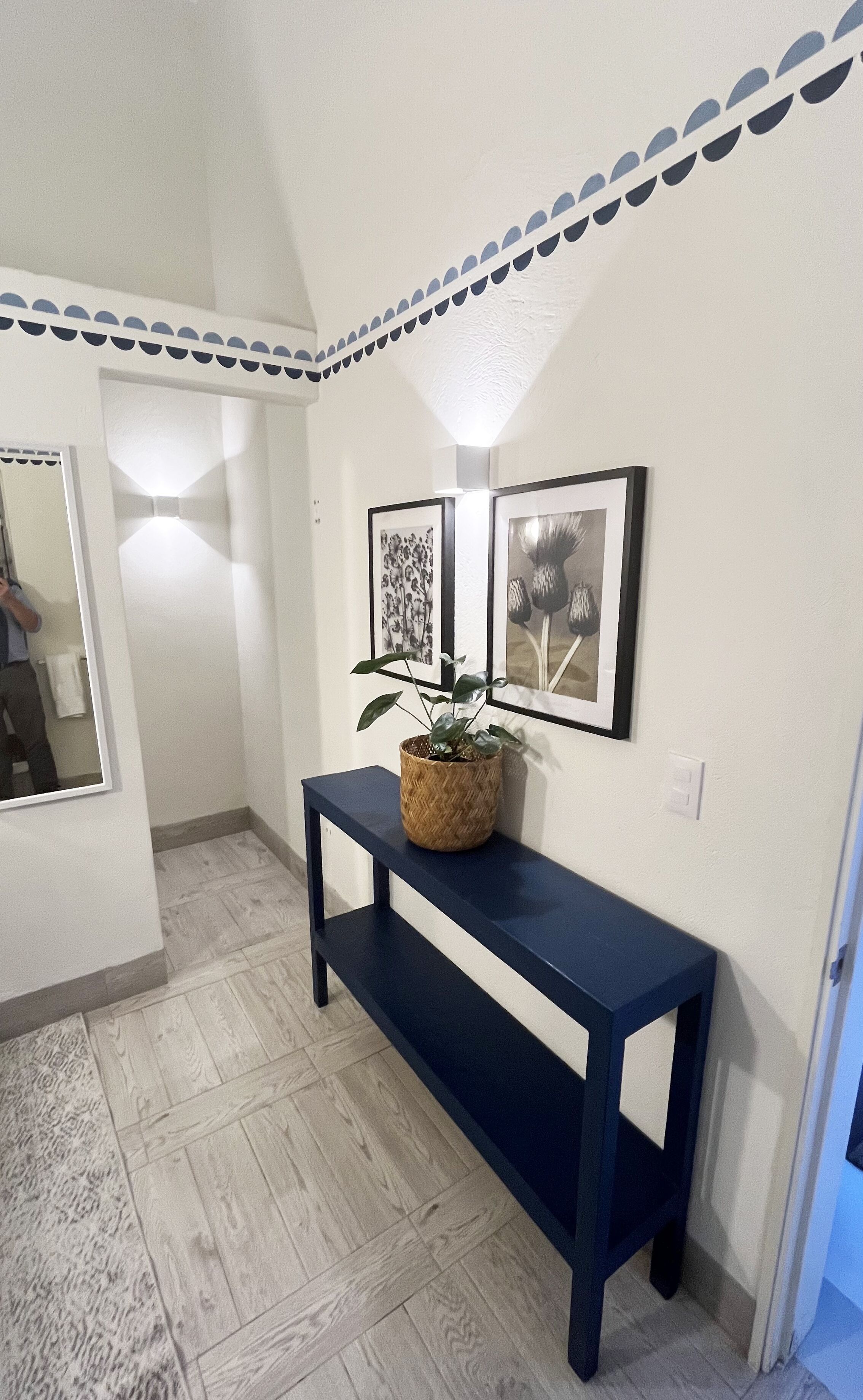 Un pasillo con una consola azul oscuro, una planta en maceta y obras de arte enmarcadas en la pared.