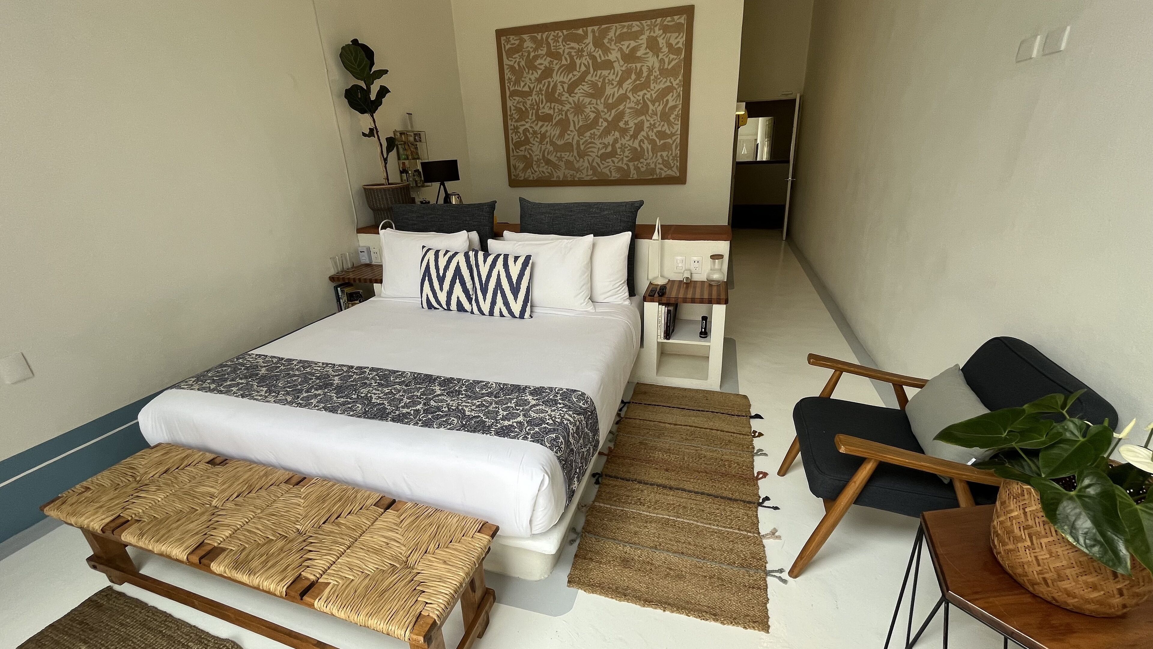 A neatly arranged bedroom with a large bed, bedside tables, a chair, and a small table with a plant.