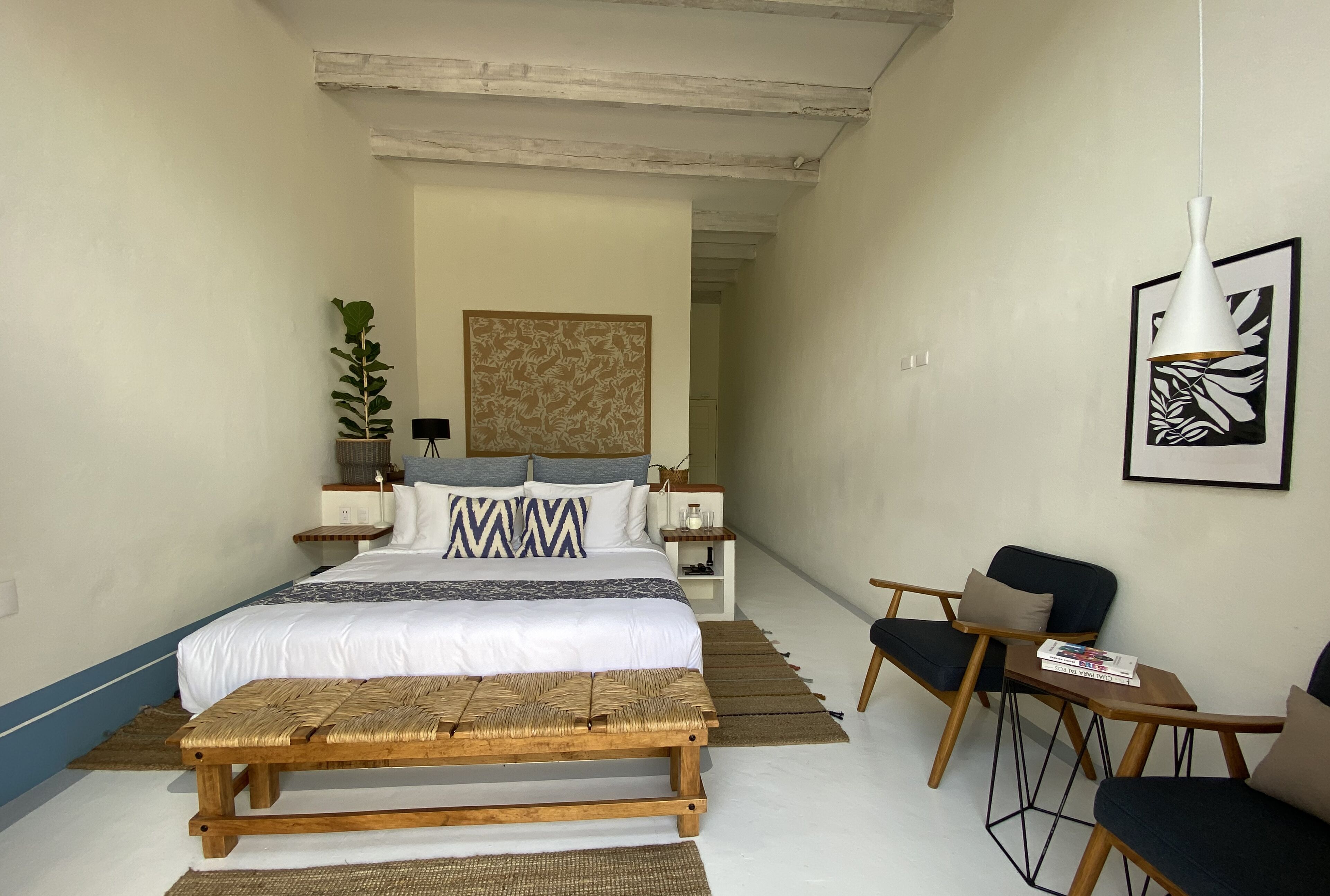 A bedroom with a bed, bedside tables, a bench, a chair, and a framed picture on the wall.