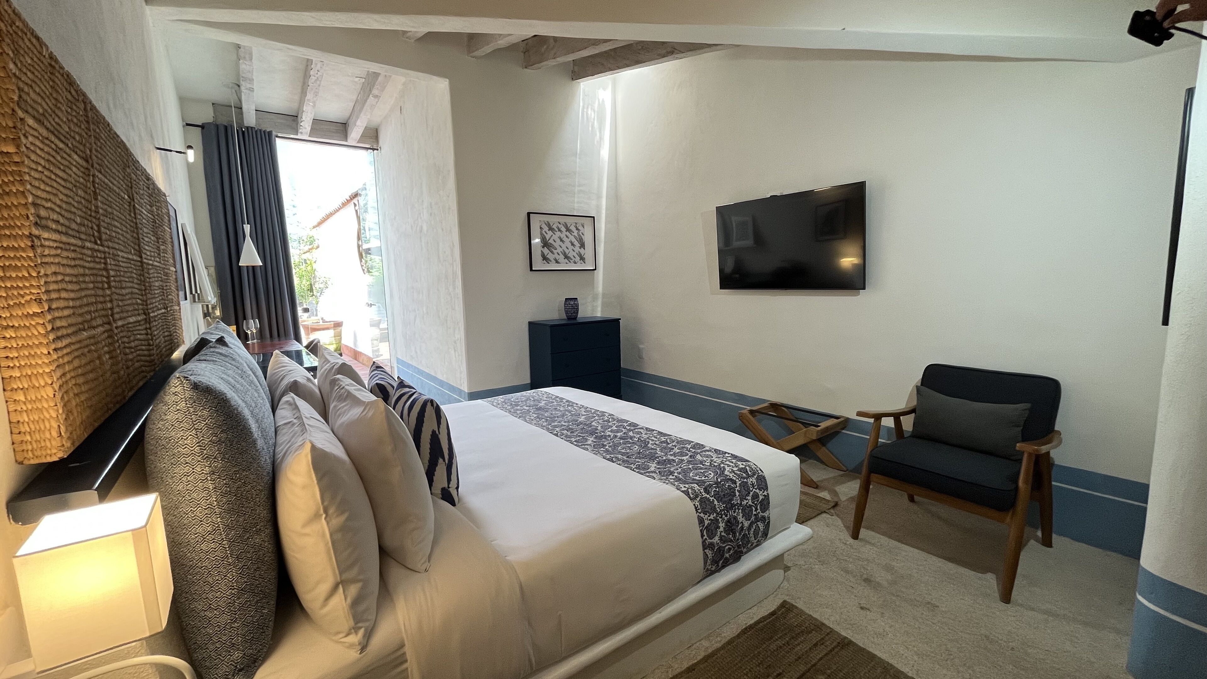A bedroom with a bed, a desk, a chair, a TV, and a window with curtains.