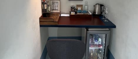 Una cocina compacta con encimera de madera, un refrigerador pequeño, una silla gris, una lámpara colgante y una ventana.