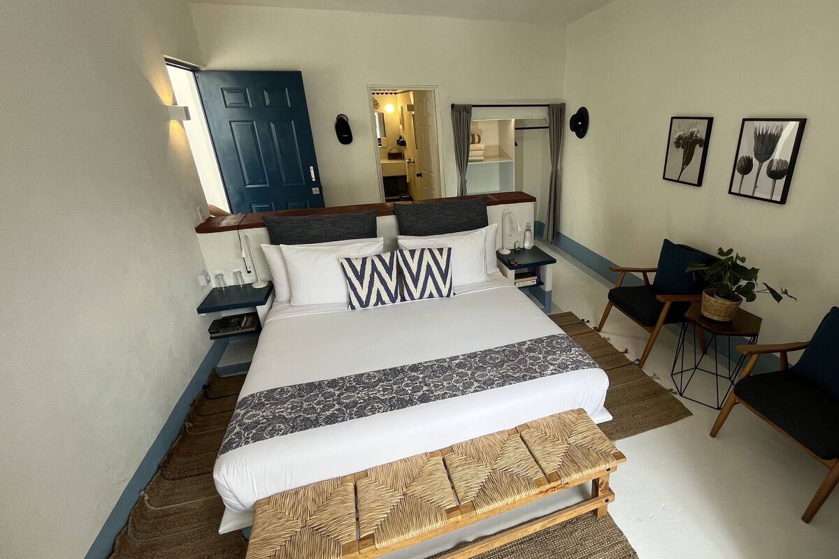 A neatly arranged bedroom with a bed, bedside tables, a chair, a small table, and a potted plant.
