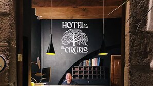 Una recepción con un letrero que dice "HOTEL EL CIRCULO" y un logotipo de árbol. Hay dos lámparas colgantes sobre el mostrador.