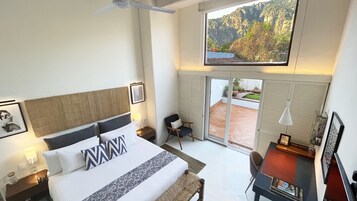 A hotel room with a bed, a desk, a chair, a TV, and a view of a mountainous landscape.