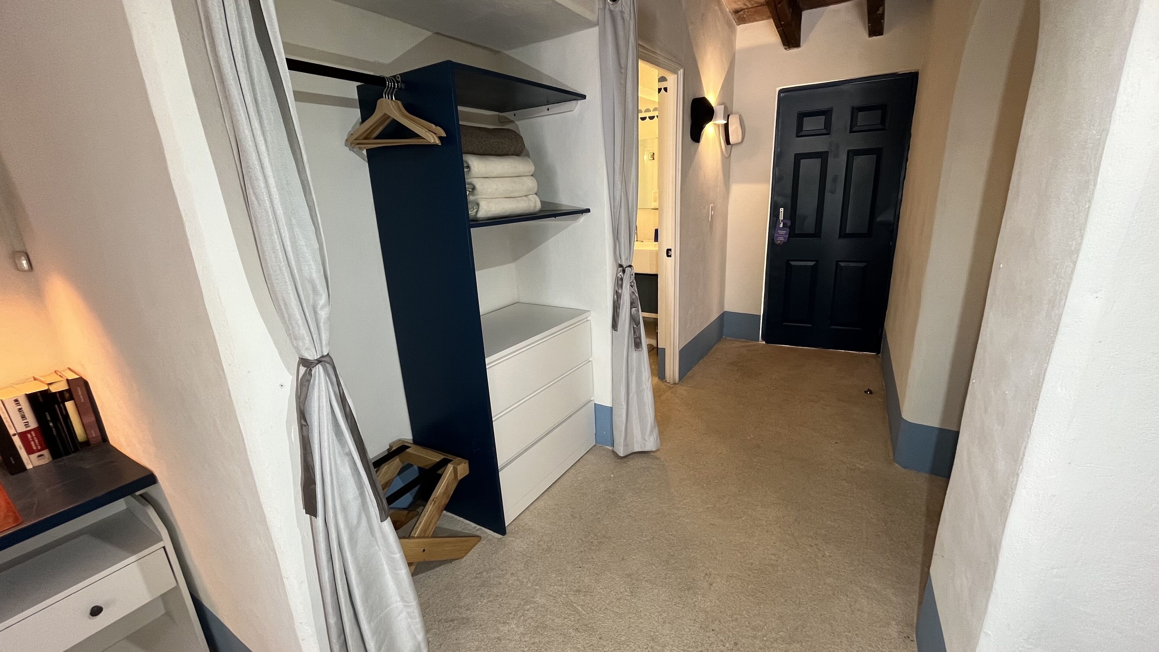 A narrow hallway with a closet containing shelves and a hanging rack, a wooden bench, and a door at the end.