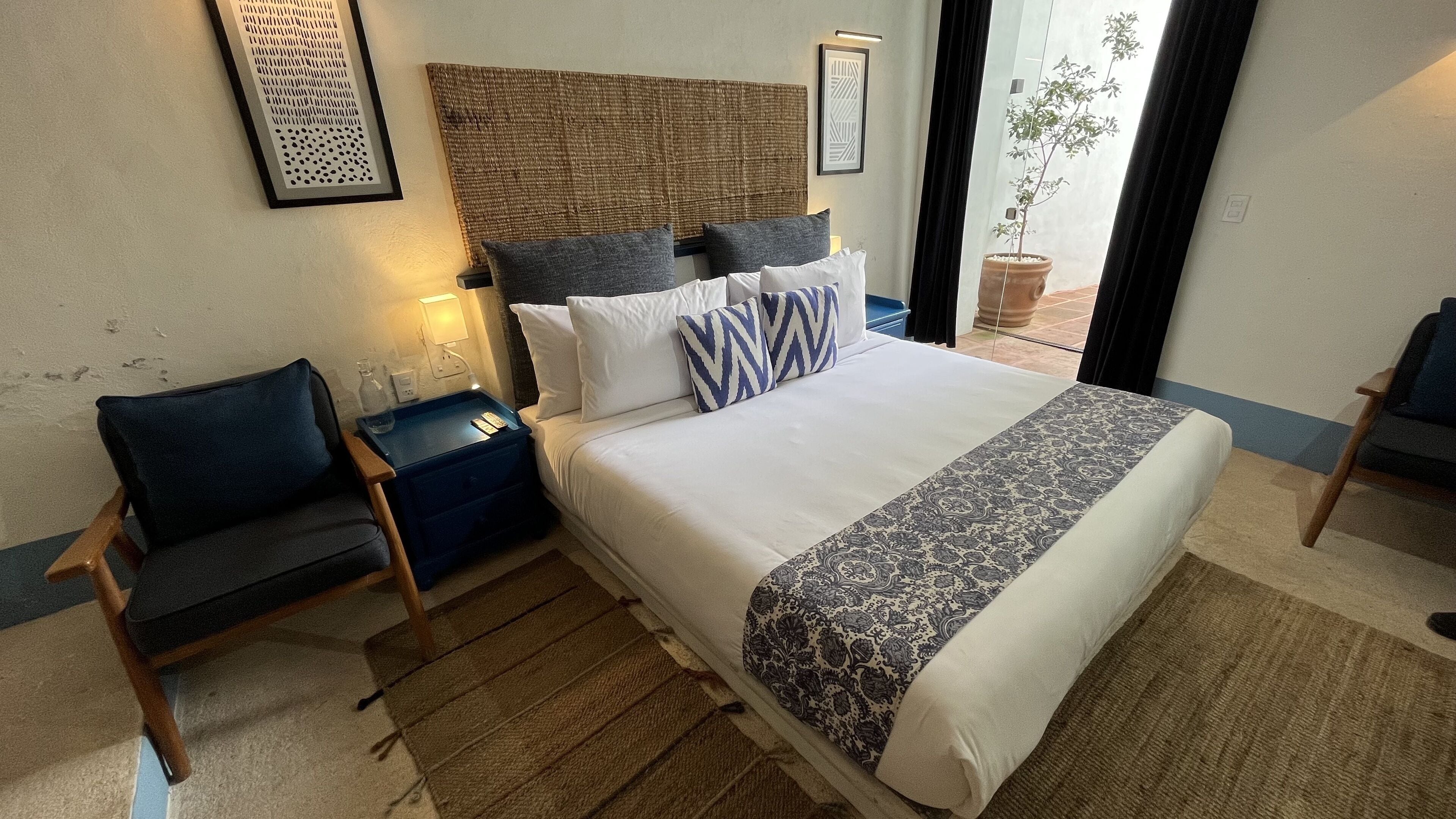 Una habitación de hotel con una cama grande, una mesita de noche, una silla y una planta en maceta.