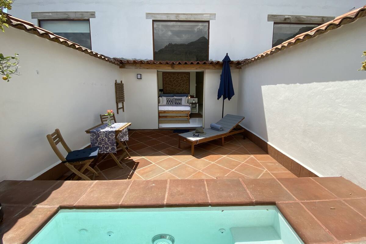A small outdoor patio with a pool, a table with chairs, and a bed with a view.