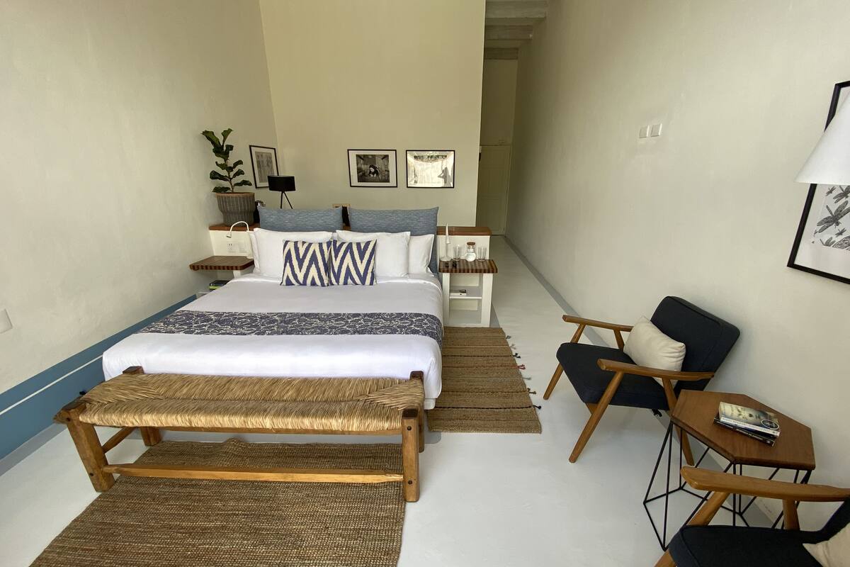 A hotel room with a bed, a bench, a chair, a small table, and a nightstand.