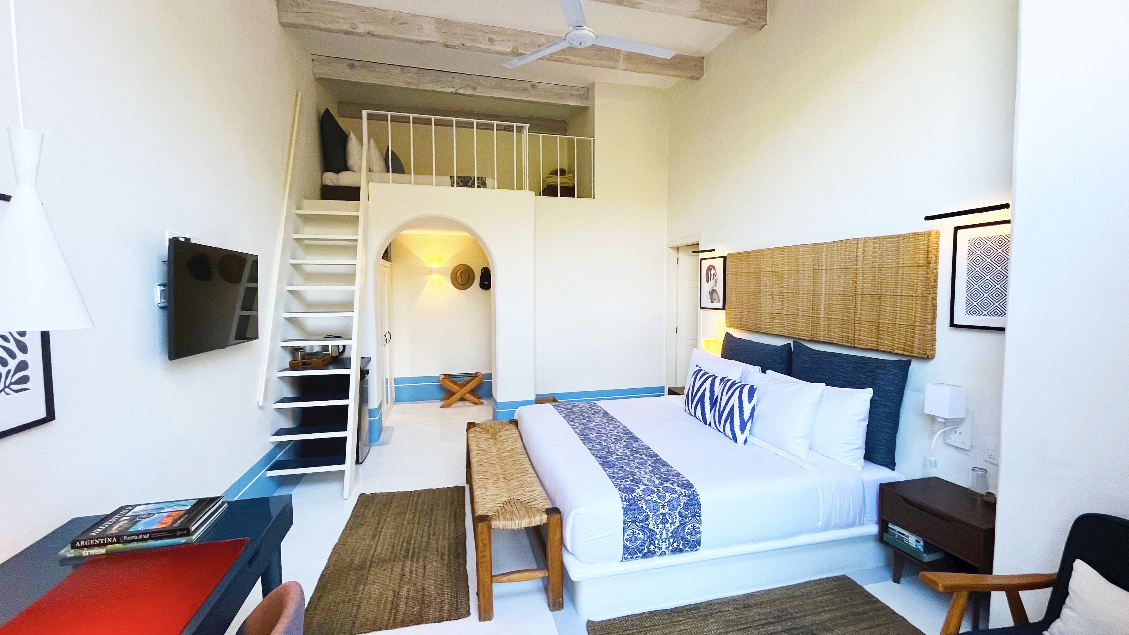 Une chambre à coucher comprenant un lit, un bureau, une chaise, un téléviseur, une bibliothèque et un escalier.