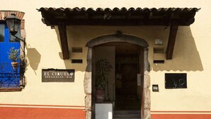 La entrada al Restaurante Bar El Ciruelo, con un arco de piedra, una puerta azul y una planta en maceta a la izquierda.