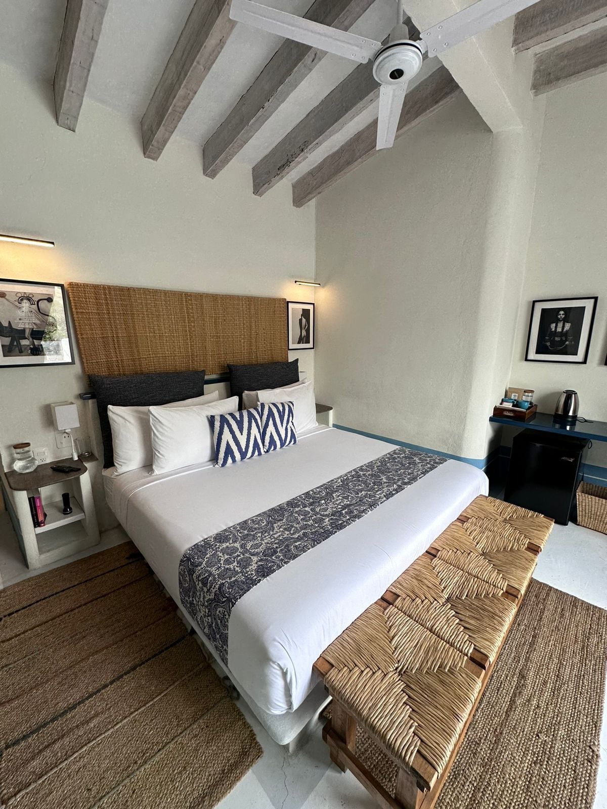 A hotel room with a bed, bedside tables, a ceiling fan, and a woven bench.