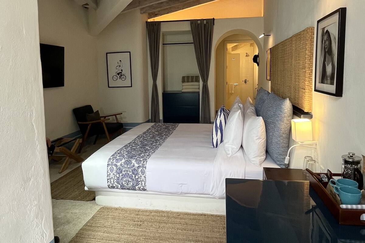 A bedroom with a bed, a desk, a chair, and a door leading to another room.