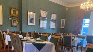 A dining area with tables set for service, framed pictures on the wall, and a chandelier. - Lovat Arms Hotel (Beauly)