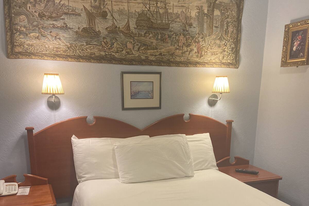 A hotel room with a large bed, two bedside lamps, a nightstand with a phone, and a wall-mounted painting.