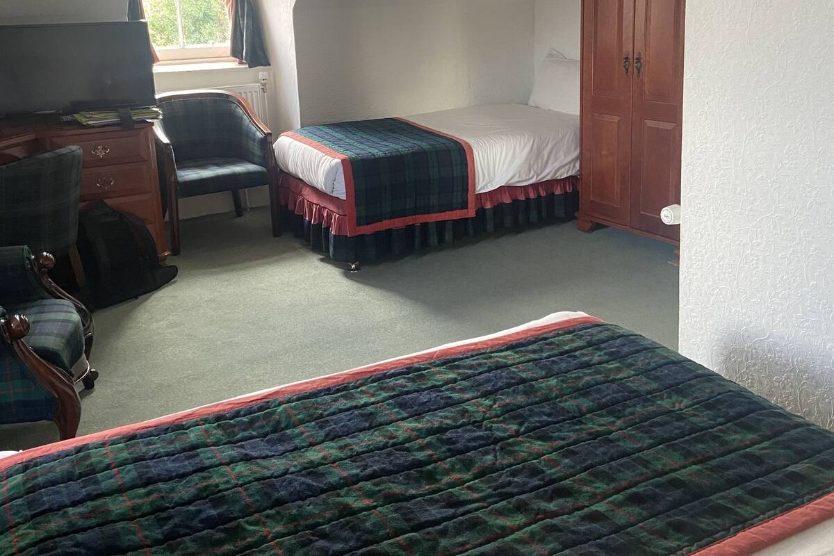 A bedroom with a bed, a desk, a chair, a wardrobe, and a window with curtains.