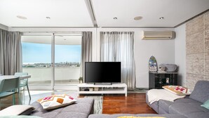 Een moderne woonkamer met een flatscreen televisie, grijze banken en een eethoek met een tafel en stoelen.