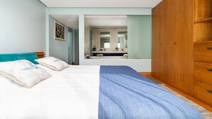 Een slaapkamer met een bed, een houten garderobe en een zichtbare badkamer door een open deur.