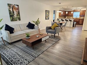 A modern living room with a sofa, armchair, coffee table, and a patterned rug.