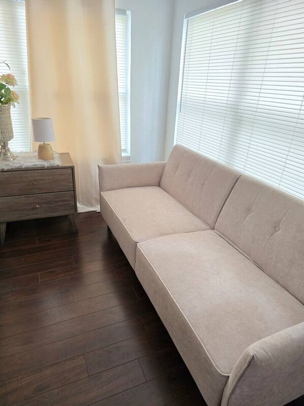 A modern living room with a beige sofa, a wooden nightstand, a lamp, and a vase with flowers.