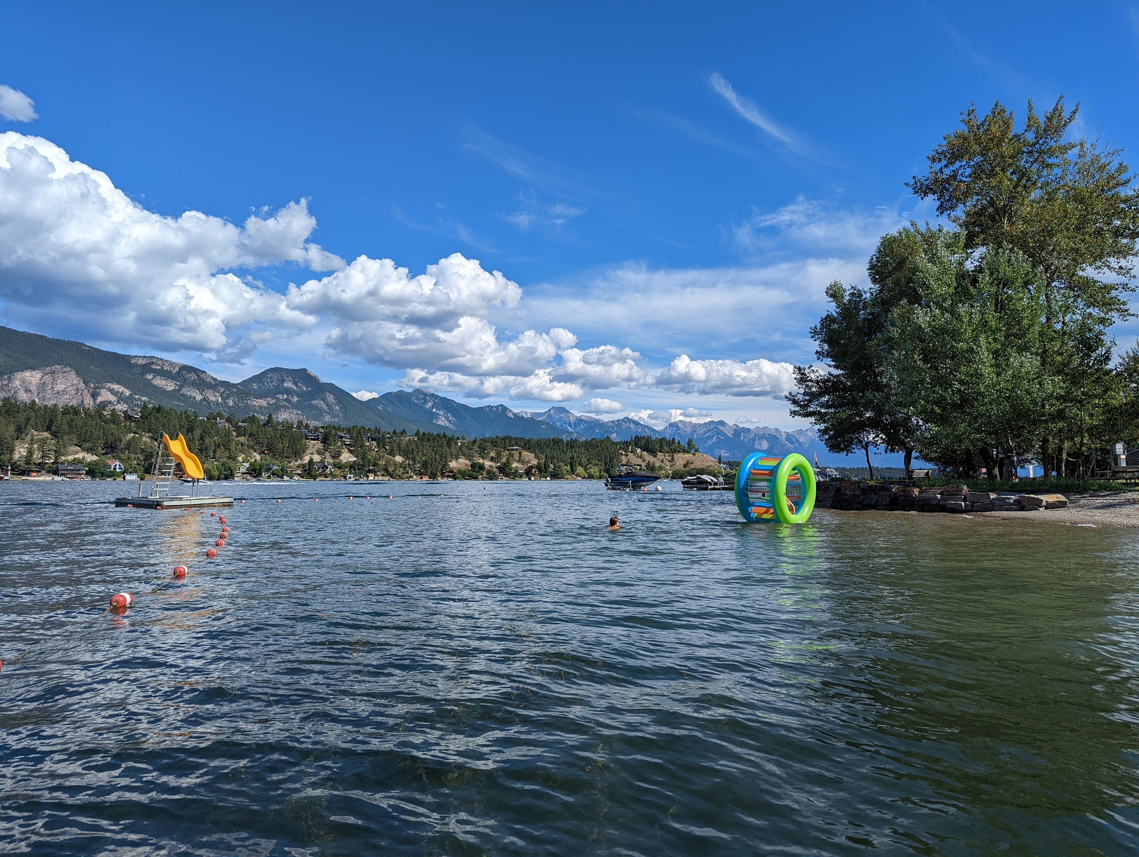 A lake with mountains in the background, a yellow floating platform, and colorful rings in the water.