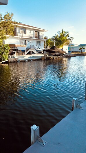 A waterfront property with a dock, a house with a balcony, and a palm tree. - Canal-Front Keys Retreat with Jacuzzi • Sleeps 12 (Big Pine Key)